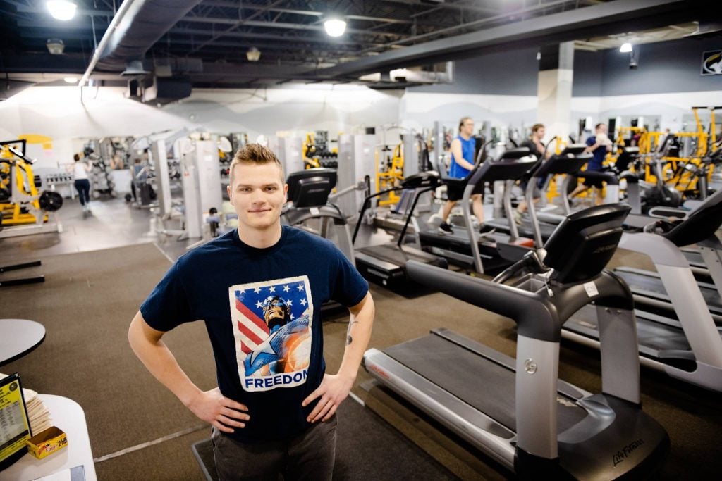A young man in a Captain America shirt stands in a fitness center.