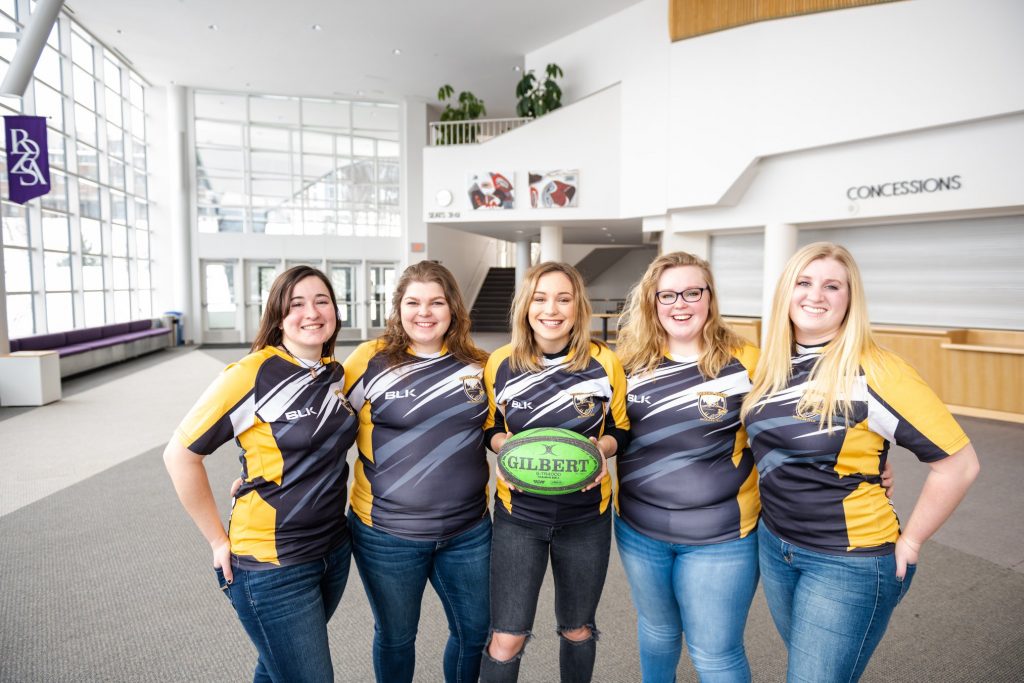 Five women in rugby shirts pose for a group photo.