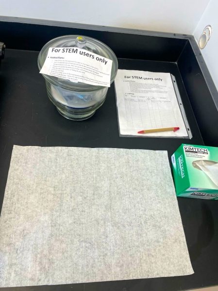 Glass desiccator jar, logbook, and wipes on a table together.