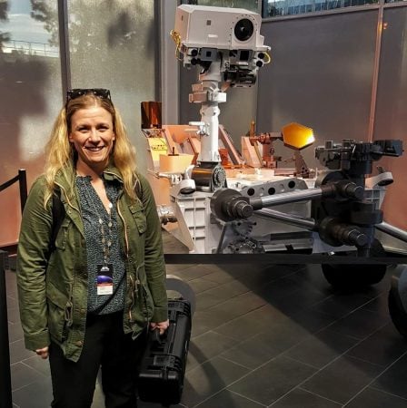 Elwell standing in front of Curiosity Rover Mockup at NASA's Jet Propulsion Laboratory holding the Solid Oxide Electrolyze for MOXIE