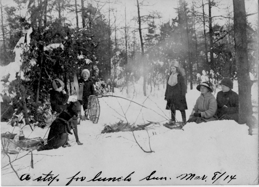 A family with their dog enjoys a picnic in the snow after snowshoeing on March 8, 1914.