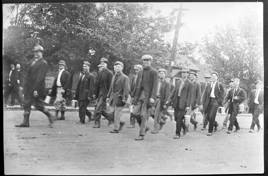 A group of almost two dozen summer field students in 1911 walking down a dirt-covered road on their way to the local mine.