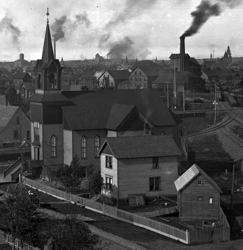 Company housing and Bethlehem Lutheran Church on Agent Street near Calumet, Michigan. The background is dominated by smokestacks, shafthouses, and other industrial workings of the Calumet and Hecla Mining Company.