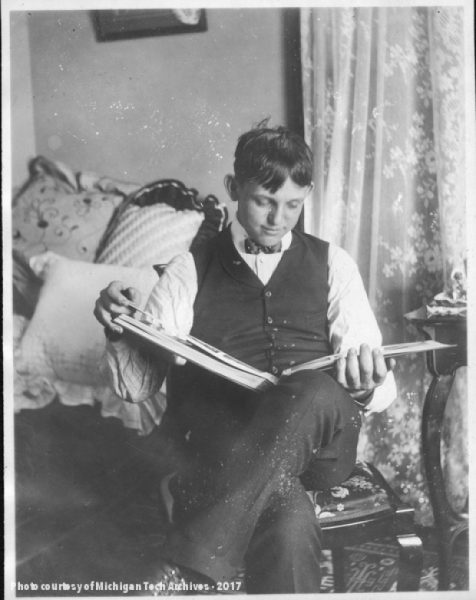 A young man is seated, reading a book.