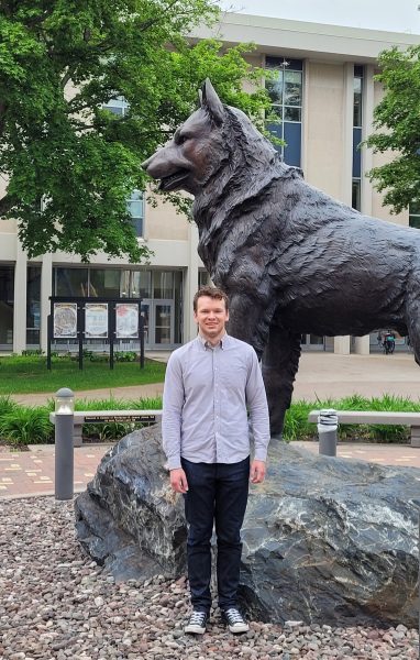 Young man in dress shirt and jeans in front of dog statue