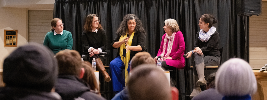 Five women sit and speak with one another in front of an audience.