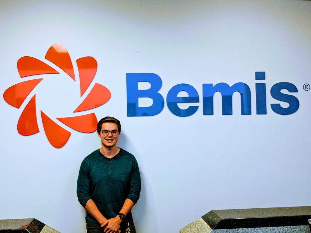 School of Business and Economics student Tom Strome stands in front of a Bemis sign/logo. 