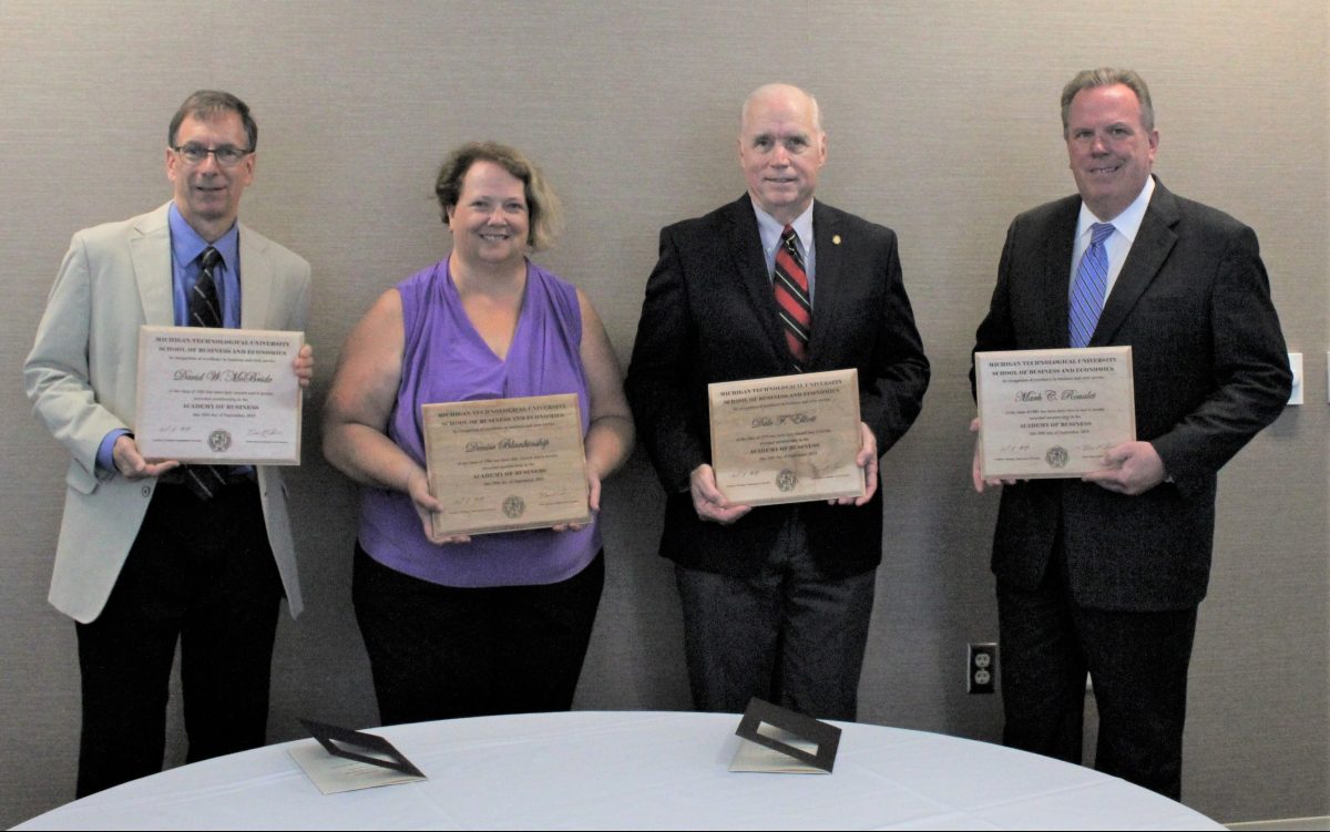 Four people stand along wall with award plaques