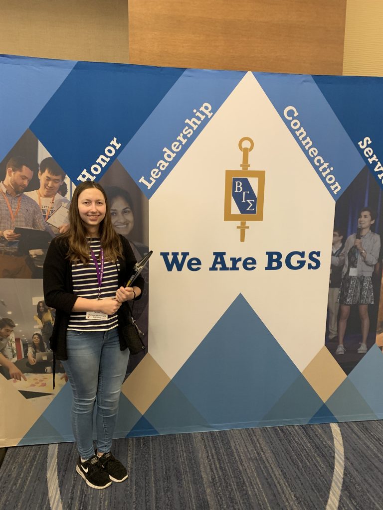 Student stands in front of Beta Gamma Sigma pull-up banner at conference.