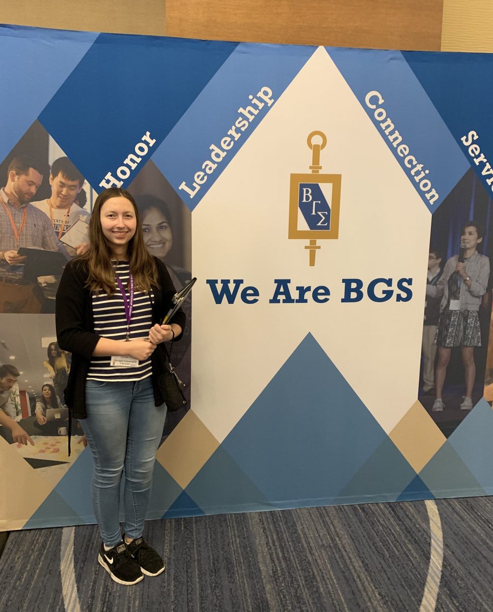 Student stands in front of Beta Gamma Sigma pull-up banner at conference. 