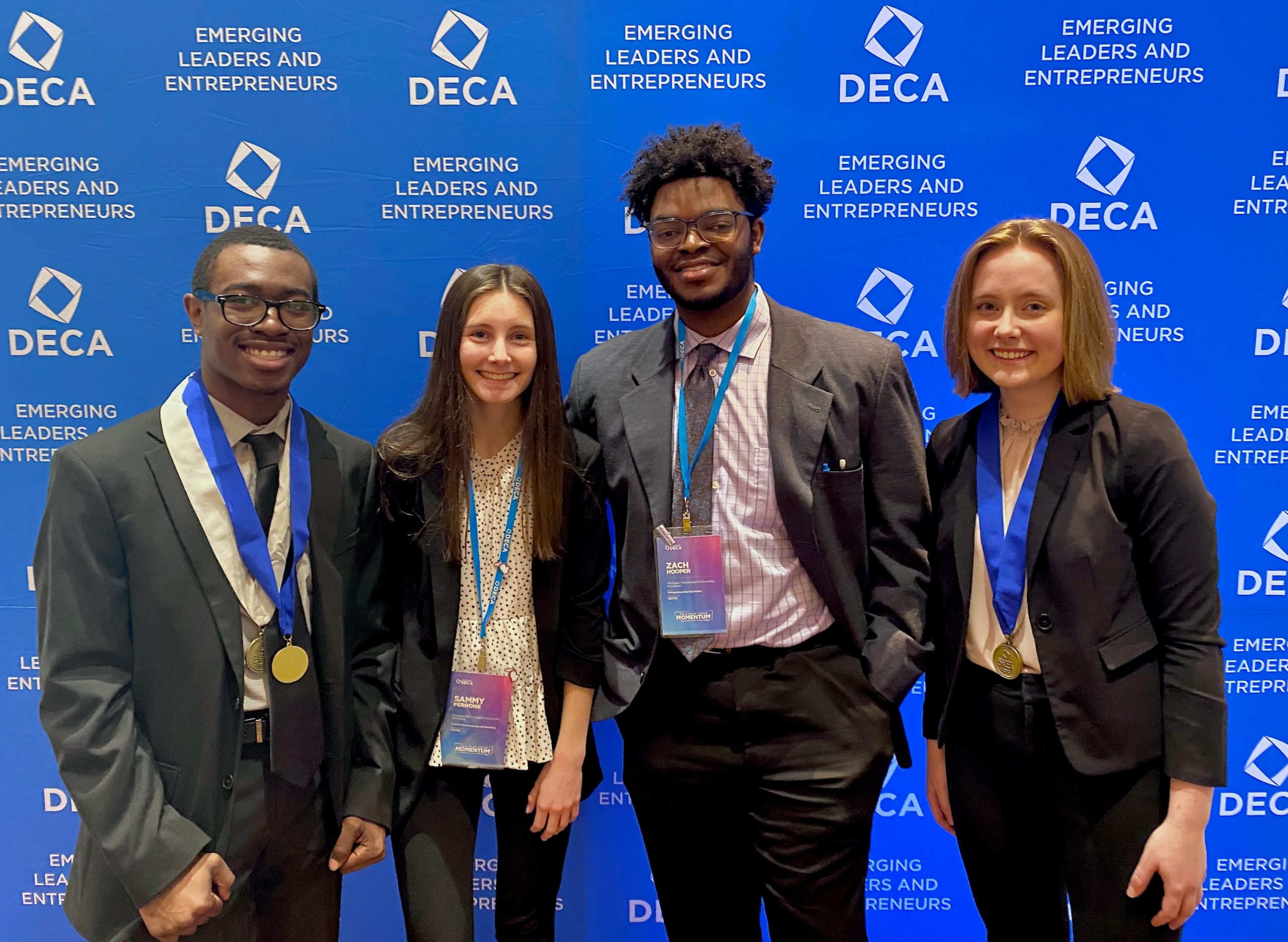 Four students stand in front of a DECA backdrop. 