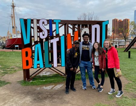 Four student stand in front of a sign in Baltimore, Maryland
