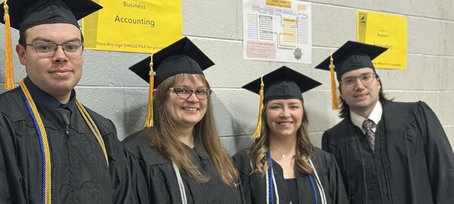 Four soon-to-be graduates stand near a sign that says Accounting in their caps and gowns at Michigan Tech graduation.