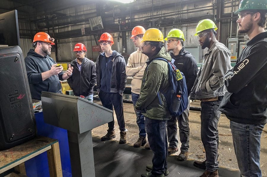 Seven Michigan Tech students in hardhats listen as a manager at Northern Hardwoods explains operations during a tour at a nearby regional lumber mill as part of a College of Business field trip.