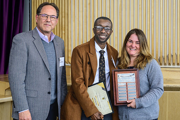 A student holds a plaque as he is congratulated by his professor and a smiling alumnus at a Michigan College of Business 2025 Student Awards Ceremony in Houghton, Michigan.