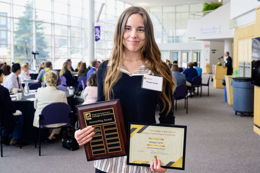 A student holds a plaque and a framed award certificate at ceremonies held in spring semester at the Rozsa Center for the Michigan Tech College of Business.
