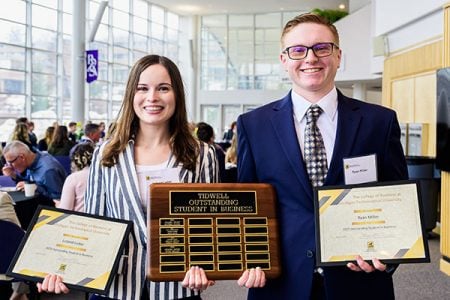 Students hold framed Outstanding Student in Business award certificates and a large wooden plaque that will bear their names after receiving the award at the annual spring semester banquet for their college at Michigan Technological University.