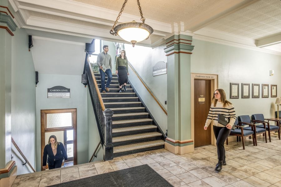 An interior shot of the Michigan Tech College of Business, with students on stairways and walking the main entrance hall, with conference room 101 in the background.