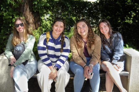 A Group of Michigan Tech female students sit on a bench together in a German Garden.