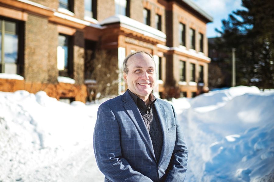 A new faculty member at Michigan Tech smiles outside in the snow with the College of Business headquarters in the Academic Office Building in the background.