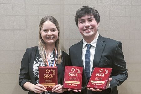 Two students hold DECA plaques at an awards ceremony and one also wears a medal around her neck.