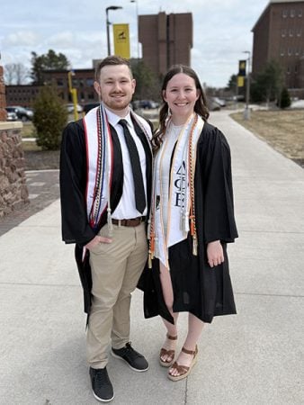 Two smiling graduates stand under the Michigan Technological University Alumni arch in April 2025 as they celebrate their achievement.