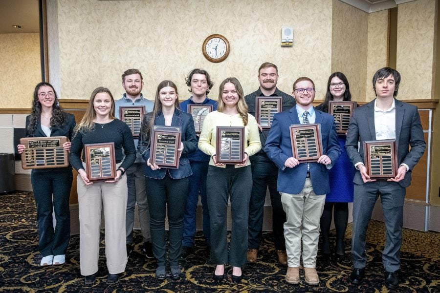 A group photo of the winners of the Michigan Tech College of Business student awards, standing in a ballroom and wearing business attire while holding plaques.
