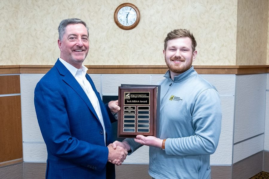 Michigan Tech student Connor Zavislak receives a plaque from alumnus Paul Stinson. They are shaking hands, and wearing business attire.