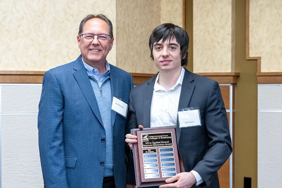 Michigan Tech student Eli Johnson receives a plaque from alumnus Kevin Wampler. Both are wearing business attire.