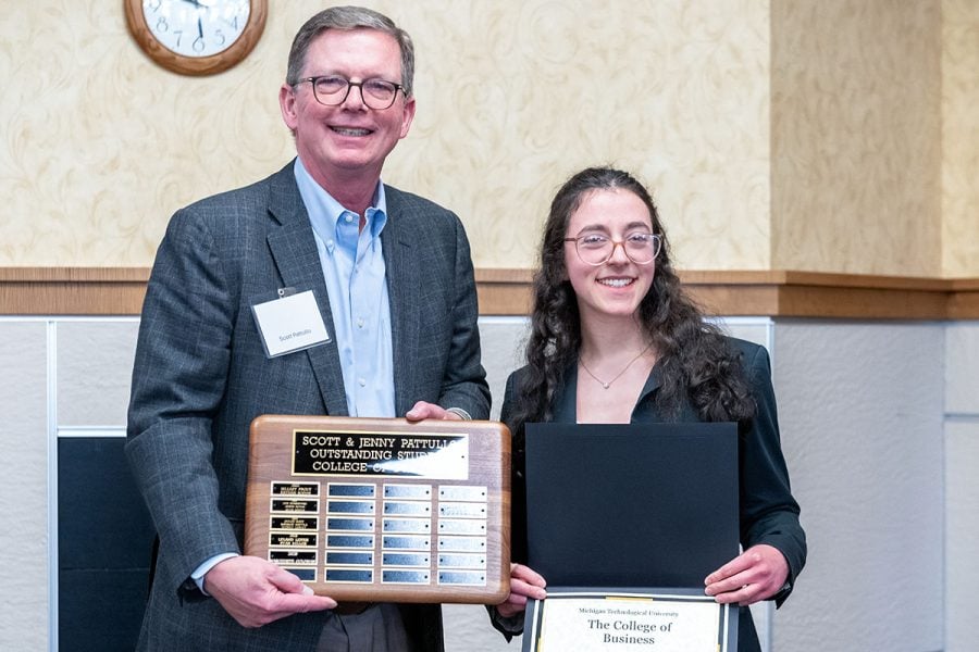 Michigan Tech student Marguerite Goldman receives an award plaque and certificate from alumnus Scott Pattullo. Both are in business attire.