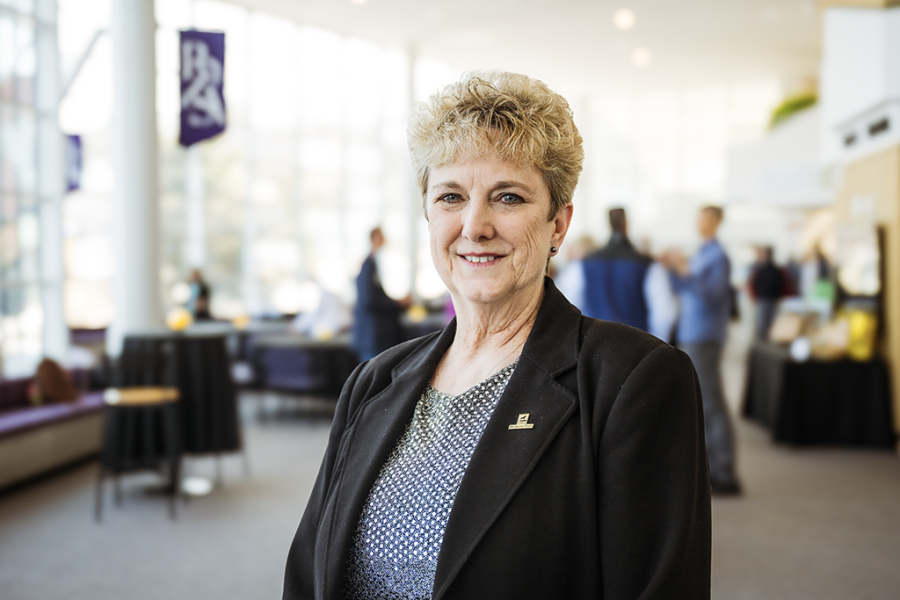 A smiling professor with a softly lit background behind her as she is honored at the Rozsa Center for the Performing Arts at Michigan Technological University.