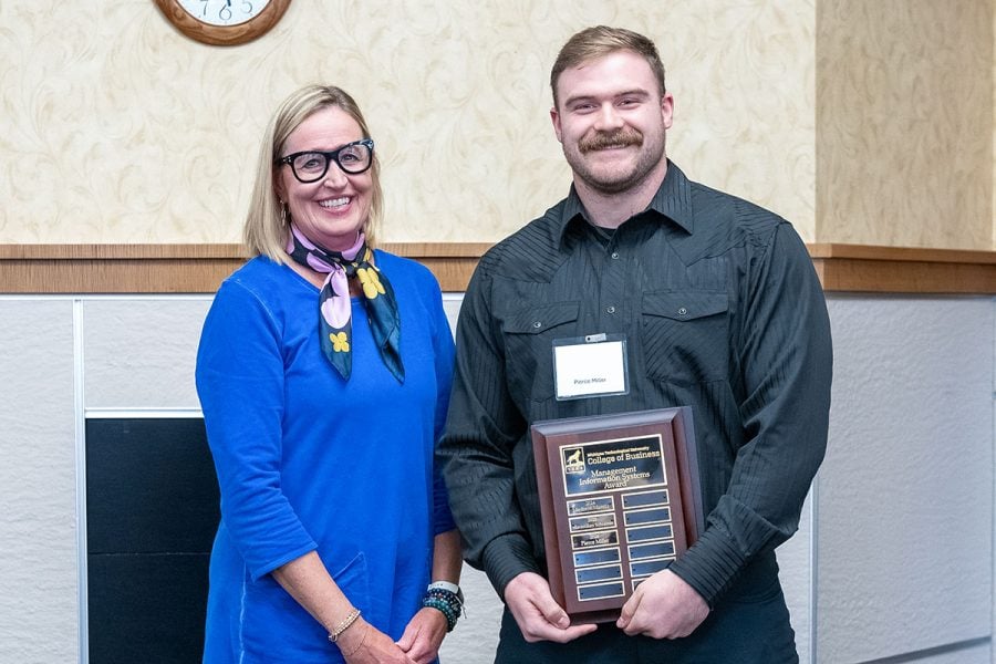 Michigan Tech student Pierce Miller receives an award plaque from alumna Carrie Schaller. Both are in business attire.