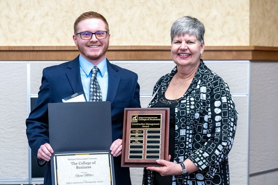 Michigan Tech student Ryan Miller receiving an award plaque and certificate from alumna Marie Cleveland. They are both in business attire.