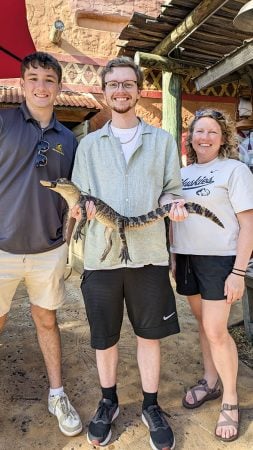 Three Michigan Tech Huskies visit an attraction where they are allowed to hold a young alligator during a competition field trip to Florida.
