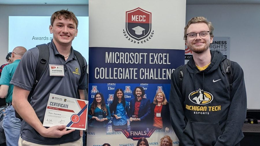 From left, Rylan Feierabend and Nick LaValley stand in front of a Microsoft Excel Collegiate Challenge board with the word “finals” and other competitors pictured on it. Feierabend is holding a third place certificate. LaValley is wearing a Michigan Tech Esports sweatshirt.