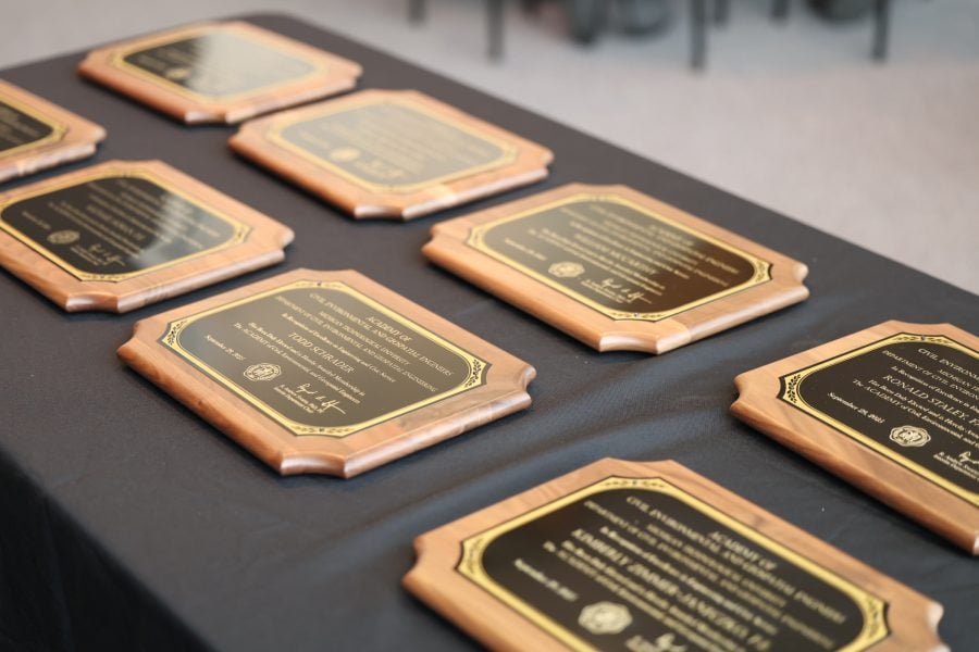 A close-up view of engraved wooden plaques displayed on a black tablecloth, each recognizing the 2025 inductees into Michigan Tech’s Civil, Environmental, and Geospatial Engineering Academy at the Rozsa Center ceremony.