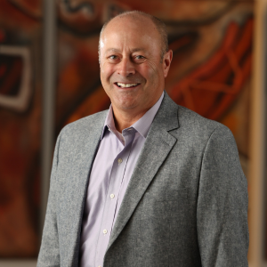 William McCarthy smiles for a professional portrait wearing a green suit jacket, white shirt, and patterned green tie, photographed against a softly blurred abstract background during the 2025 CEGE Academy Induction Ceremony at Michigan Tech.