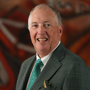 William McCarthy smiles for a professional portrait wearing a green suit jacket, white shirt, and patterned green tie, photographed against a softly blurred abstract background during the 2025 CEGE Academy Induction Ceremony at Michigan Tech.