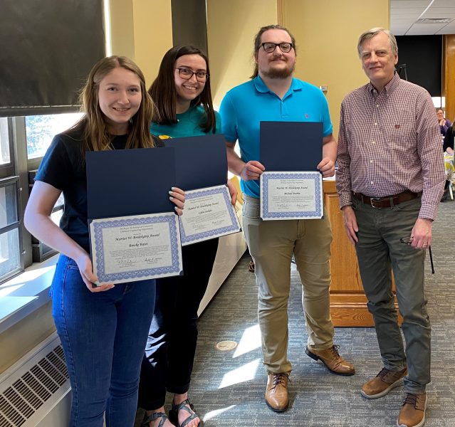 Three students holding awards and a faculty member.