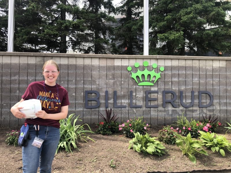 Katherine holds a helmet and stands in front of the Billerud company entrance sign.