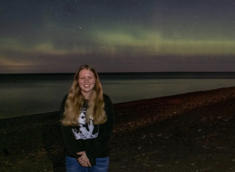Lauren stands at the shore of Lake Superior at night with Northern Lights in the background.
