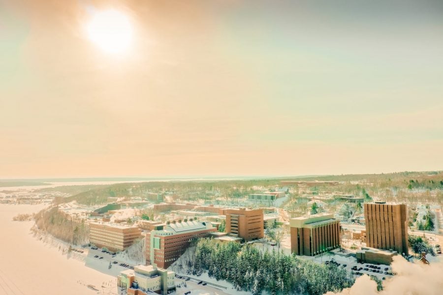 An aerial drone image of campus in the snow with pink sunlight at sunrise.