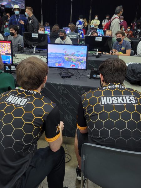 An image of Ryan and another Esports member, at a competition. They are facing away from the camera and at a screen.
