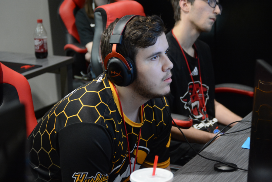 Ryan Mackie during a Esports competition. He is seated, wearing headphones and a Michigan Tech Jersey.