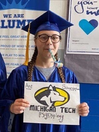 New student Ani Schneiderhan at high school graduation holding a "Michigan Tech" sign.