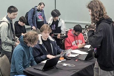 Eleven students sit at long conference tables in front of their laptops and with other hacking tools in front of them as they compete in a cybersecurity challenge for Michigan Tech at CypherCon in Wisconsin.