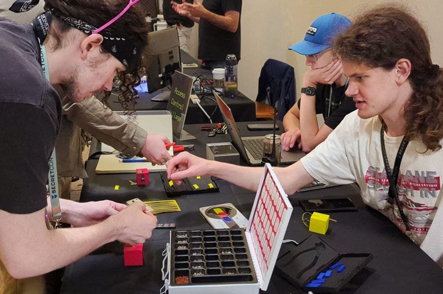 A close-up of four Michigan Tech students intently working on a key matching collection, a laptop, and other assorted tools used as part of red teaming for cybersecurity hacking competitions.