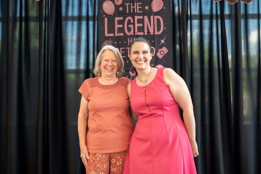 Linda Ott and Brianna Betin standing in front of a sign that says "The Legend has Retired".