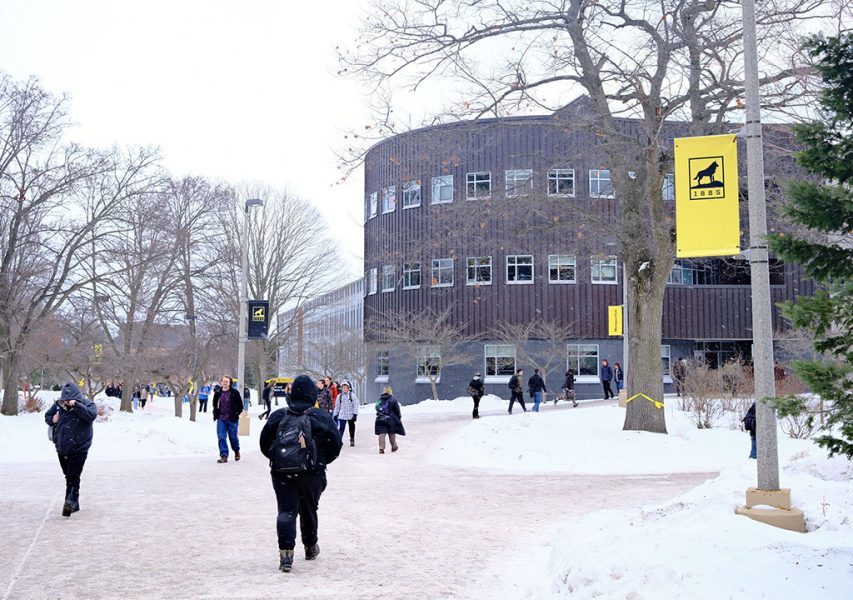 A snowy campus scene of students heading to class with Michigan Tech signs outside Rekhi Hall.