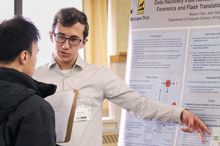 A Michigan Tech computer science student explains his research to a faculty member while gesturing at a poster related to “Data recovery from ransomware, forensics, and flash translation.”